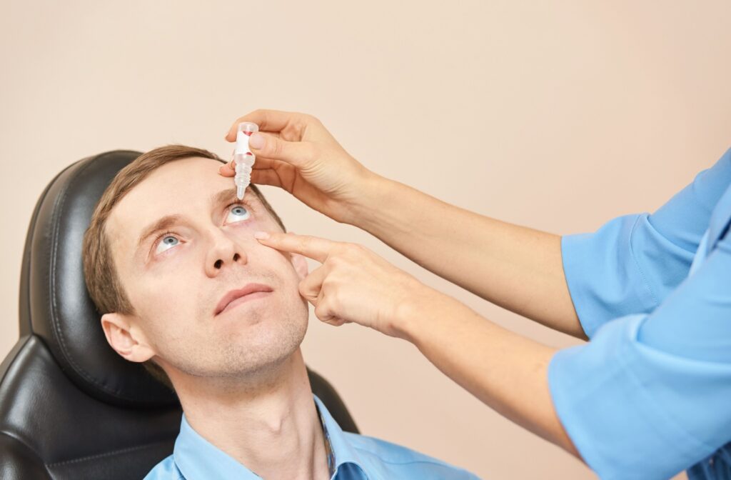 An off-screen optometrist carefully applies eye drops to a male patient's eye.