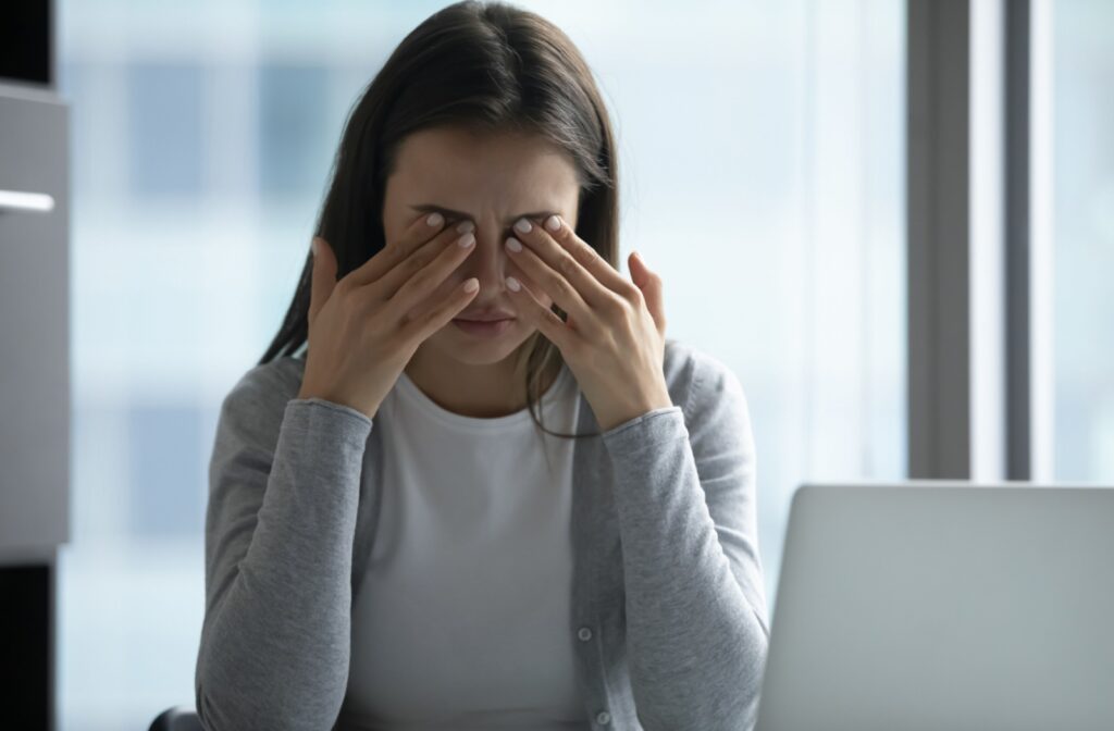 A young woman taking a break from her computer to rub her burning eyes with both hands.