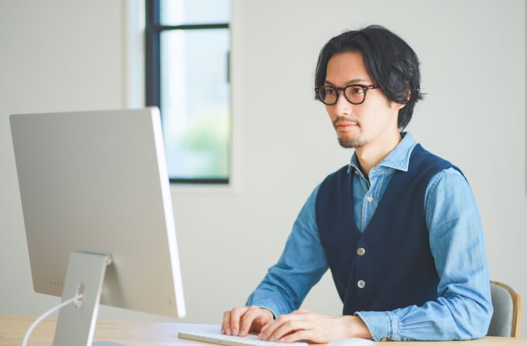 A young man sits at his computer with good posture in a well-lit room.