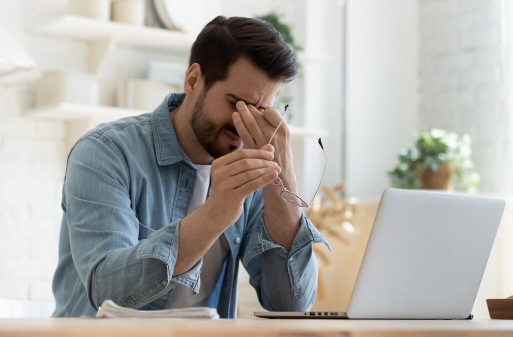 A young man at his computer rubbing his burning eyes in frustration.