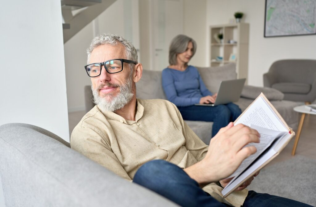 A person wearing reading glasses looks up from their book and gazes out the window.