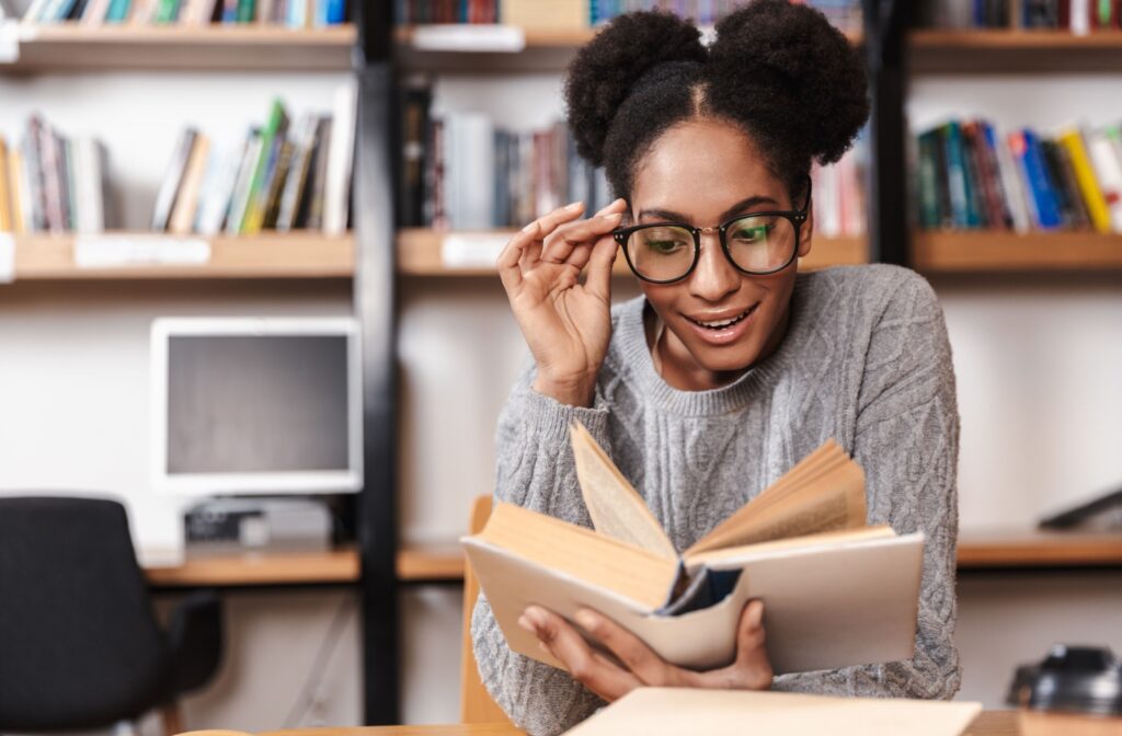 A person adjusts their glasses as they read a book in the library.