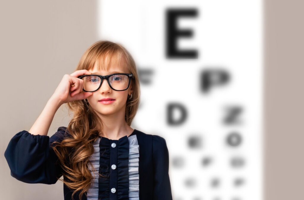 A child standing in front of a blurry eye chart adjusts their glasses.