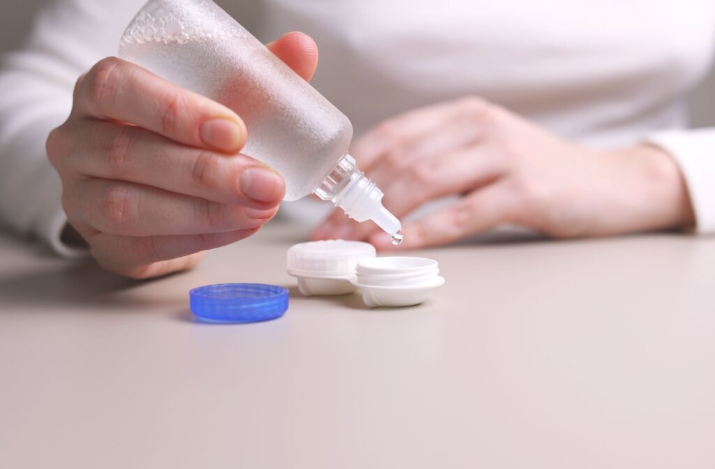 A hand adds solution to a contact lens case on a table.