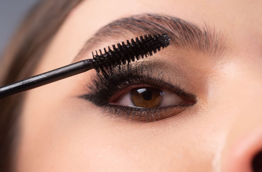 A close-up of a person with shimmery eyeshadow applying mascara.