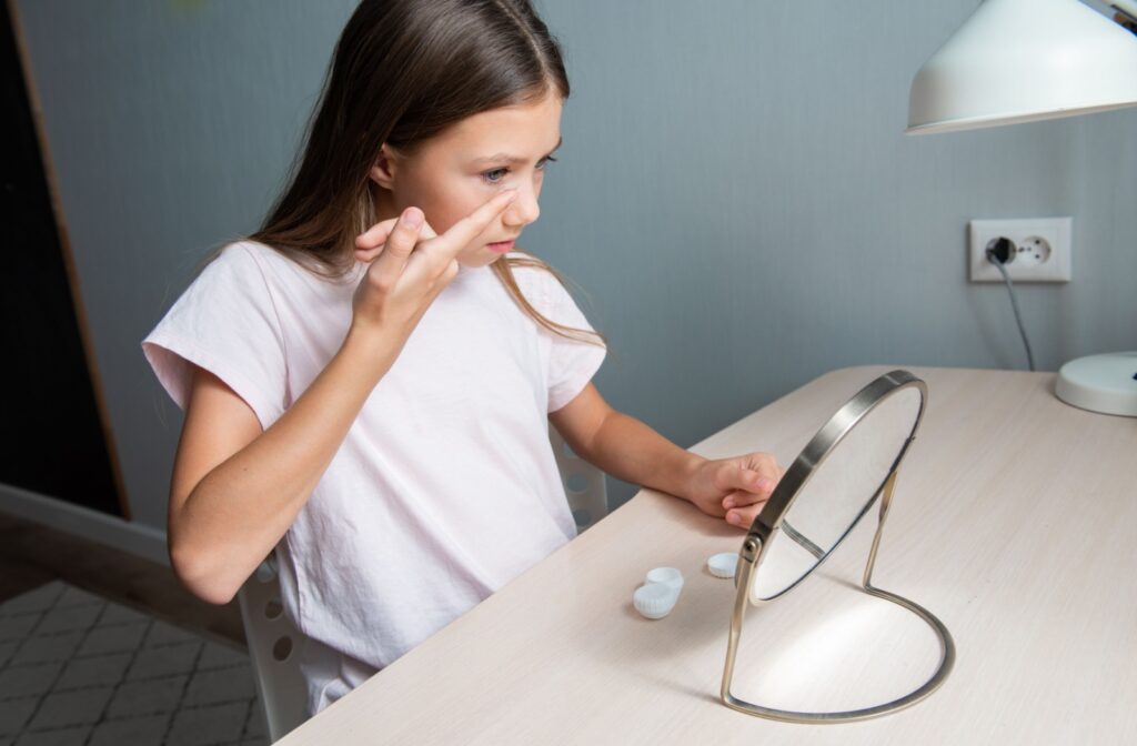 A child looking in a mirror, inserting a contact lens into their eye to help correct their myopia.