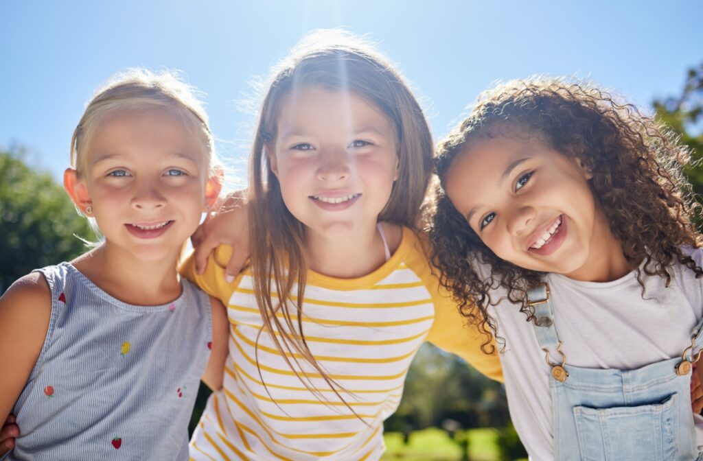 Three kids smiling, spending time outdoors to help prevent the progression of myopia.